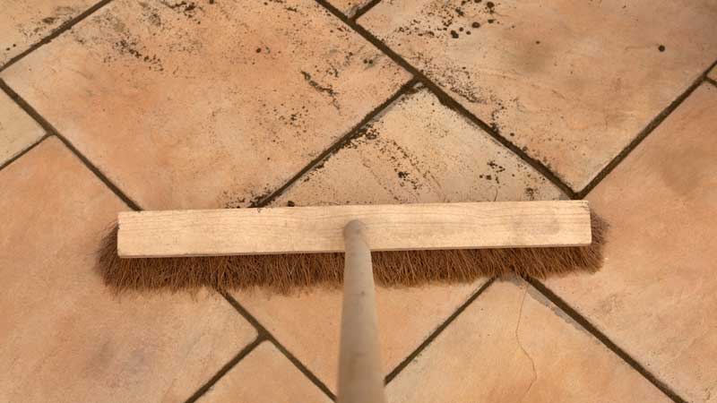 Patio being cleaned by a push broom and water