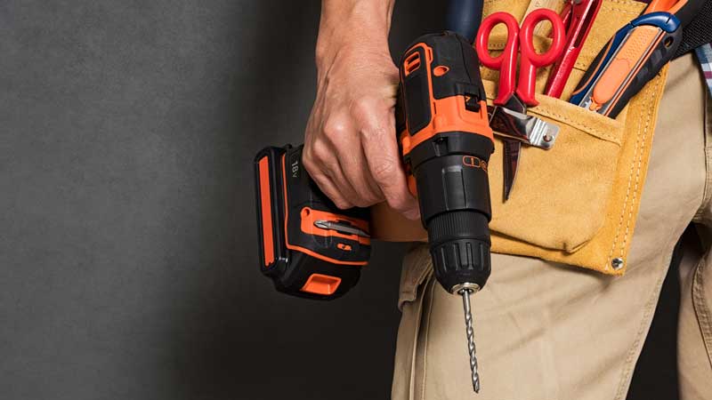 Handyman holding a drill with bit and toolbelt.