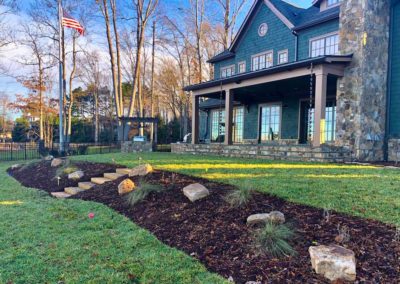 Rear of Lakeside house in the Charlotte area with landscaping bed, stone steps, patio and grill by Benton Outdoor Living