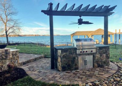 Rear yard of lakeside home in the Charlotte area with paver patio, grilling island with pergola and a view of the lake