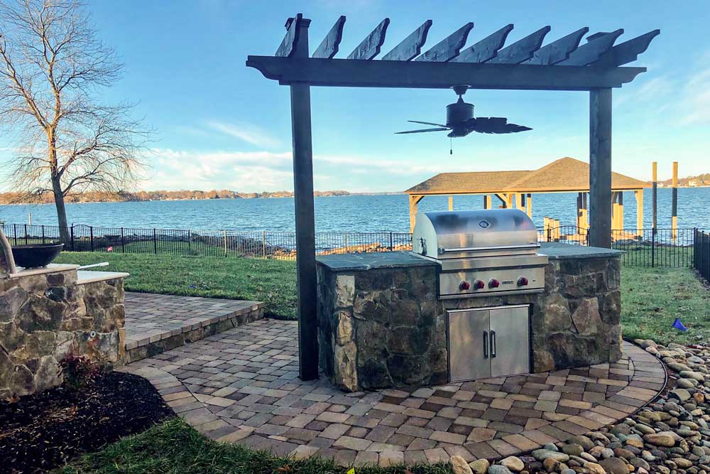 Rear yard of lakeside home in the Charlotte area with paver patio, grilling island with pergola and a view of the lake