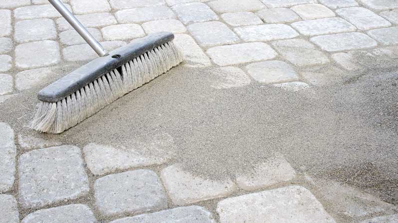 Brooming polymeric sand into pavers to help lock them together and form a bond much like one would do with grout for tiles.