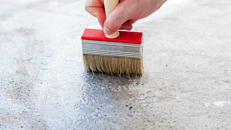 hand with paint brush putting stain on a piece of concrete.