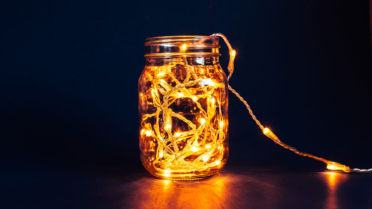 Mason jar with string of electric lights inside as an outdoor lighting idea for a table.