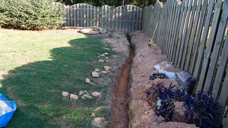 French drain trench in yard along fence for better drainage