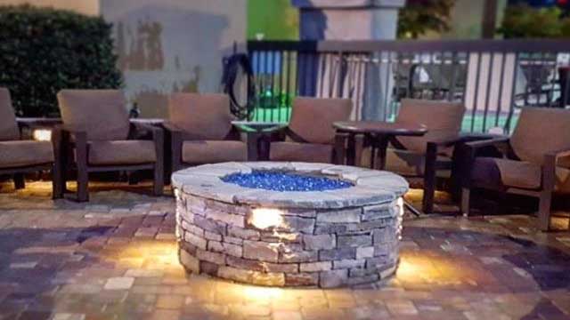 Gas fire pit with seats surrounding it near a pool
