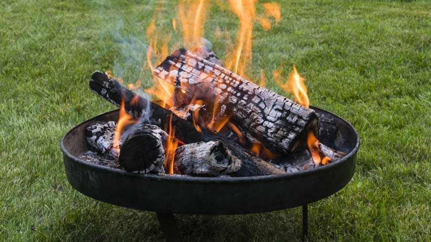 Flames and fire in a portable fire pit that is sitting on the grass in the yard