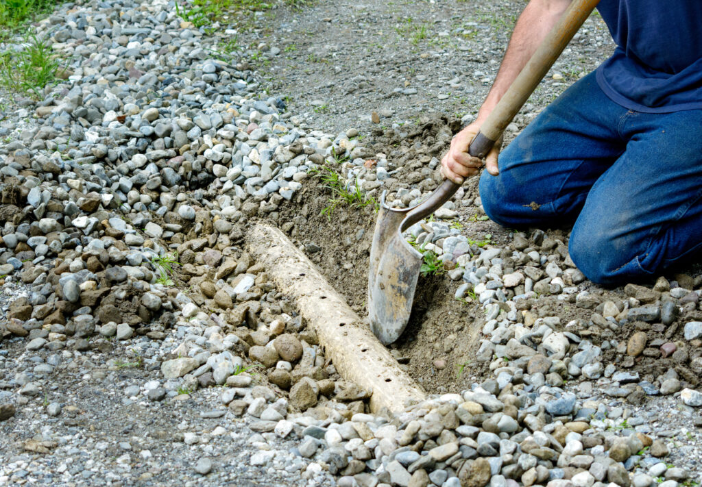 Man digging to find a french drain that has failed because it has clogged in his yard.
