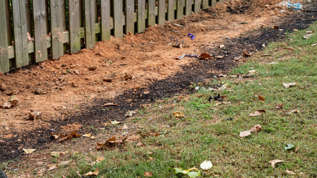 french drain along fence covered by soil and ready to have grass grow back over it.