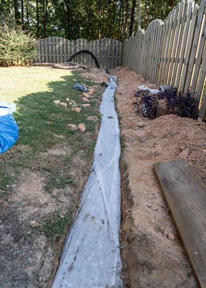 Trench for french drain along a fence line in a backyard