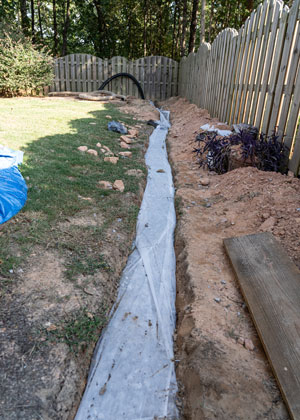 Trench for french drain along a fence line in a backyard