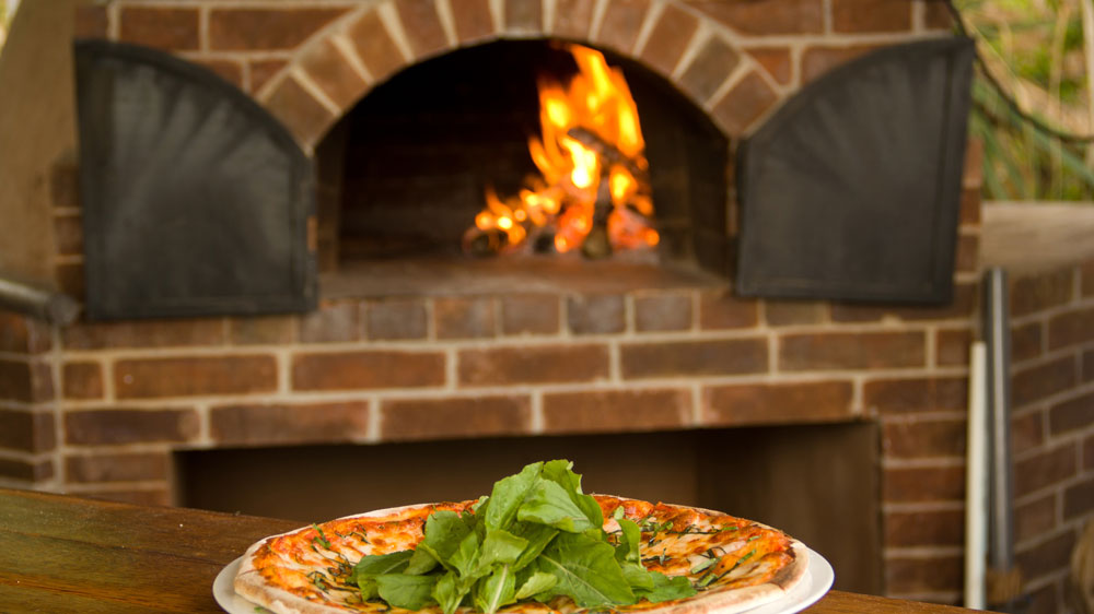 Outdoor fireplace with Pizza oven built above it and pizza sitting on the table.