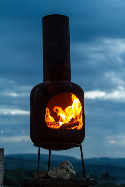 Chiminea with a lit fire burning against the background of a dark sky.