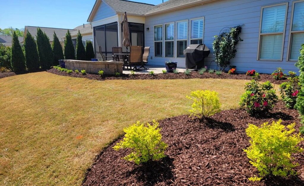 Fort Mill backyard landscaping with patio, seating wall, landscaping plants and privacy screening.