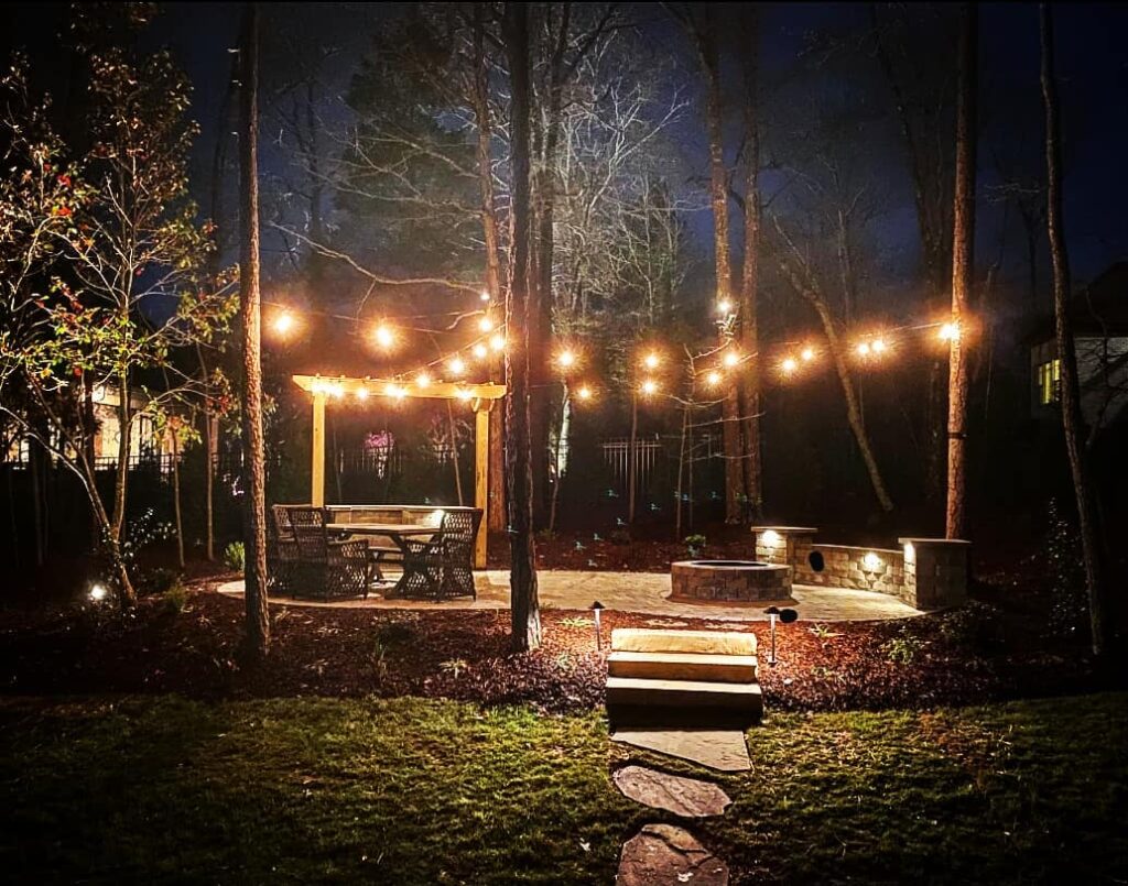 Outdoor wooded patio area with string lighting and low-voltage lights around the edges to make it a safe and inviting location during the night.